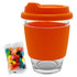 A clear glass coffee cup with an orange silicone sleeve and lid, accompanied by a pack of colourful jelly beans.