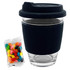 A clear glass coffee cup with a black silicone sleeve and lid, alongside a pack of colourful jelly beans.
