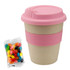 A bamboo cup with a pink lid and band, accompanied by a bag of colourful jelly beans.