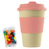 A reusable 12oz bamboo cup in beige with a pink silicone sleeve, accompanied by a pack of colourful jelly beans.