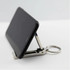 A black phone propped up by a silver mobile stand and hanger key ring, showcasing its compact design.
