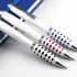 Three metal pens in white with patterned grips in red, blue, and black, resting on a notebook. Each pen features a logo.