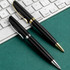 Two sleek black metal pens with silver and gold accents are placed next to a keyboard on a green surface.