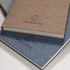 A brown and a blue notebook stacked, featuring a logo. Both have a textured cover and a simple design.
