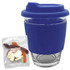 A reusable glass coffee cup with a blue silicone lid and sleeve, accompanied by a pack of jelly candy.