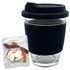 A reusable clear glass coffee cup with a black silicone sleeve beside a packet of jelly sweets.