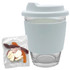 A reusable coffee cup in clear glass with a light blue silicone sleeve, accompanied by a pack of jelly candies.
