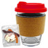A glass coffee cup with a cork band and a red lid, accompanied by a pack of mixed lollies.