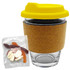 A glass coffee cup with a cork band and yellow lid, accompanied by a bag of mixed lollies in various colours.