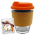 A glass coffee cup with an orange lid and cork band, accompanied by a bag of mixed lollies in various colours.