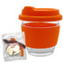 A clear glass coffee cup with an orange silicone lid and sleeve, accompanied by a bag of mixed jelly lollies.