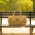 A kraft paper duffle bag in a tan colour sits on a park bench, featuring handles and a logo.