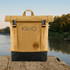 A kraft paper laptop backpack in tan and black, featuring straps and a logo, set against a scenic river backdrop.