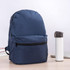A navy blue backpack with a front zip pocket beside a white drink bottle on a desk.