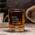 A glass tumbler filled with amber liquid, featuring a clear branding logo, set on a wooden surface.