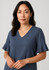 A woman wearing a dark blue blouse with fluted sleeves and a v-neckline, featuring a simple design and soft fabric.