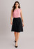 A woman is wearing a pink blouse with a black flared skirt, standing in a neutral background. The skirt has a smooth finish and a logo.