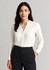 A white long sleeve blouse with a collar, worn by a woman, paired with dark trousers. Branding is present.