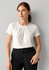 A woman wears a white short sleeve top with a pleat design, paired with black trousers and holding a clutch.