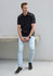 A man wearing a black short sleeve polo shirt with contrasting white accents, paired with light jeans and black sneakers.