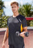 A black and yellow short sleeve tee featuring a logo, model holding a dumbbell in an outdoor setting.