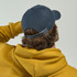 A navy cap with an adjustable strap, worn by a person in a yellow hoodie, viewed from the back.