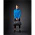 A woman wearing a bright blue lightweight softshell jacket holds a black duffel bag against a dark background.