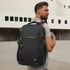 A grey backpack with green zippers is being worn on one shoulder by a man outdoors. The backpack has a logo.