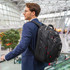 A man in a suit carries a black Swissdigital Pixel Backpack, standing in an expansive indoor space.