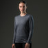 A woman wearing a long-sleeve grey t-shirt stands against a dark background. The shirt features a logo.