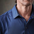 A close-up of a men's blue striped polo shirt featuring a collar and button details. The shirt has a logo on it.