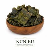 An elegant wooden bowl filled with whole dried Kun Bu (Laminaria japonica) sits centered on a clean white background. The herb consists of naturally curled, irregular pieces ranging in color from olive green to deep brown with a slightly wrinkled texture, highlighting its minimally processed, whole-herb appearance.