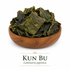 An elegant wooden bowl filled with whole dried Kun Bu (Laminaria japonica) sits centered on a clean white background. The herb consists of naturally curled, irregular pieces ranging in color from olive green to deep brown with a slightly wrinkled texture, highlighting its minimally processed, whole-herb appearance.