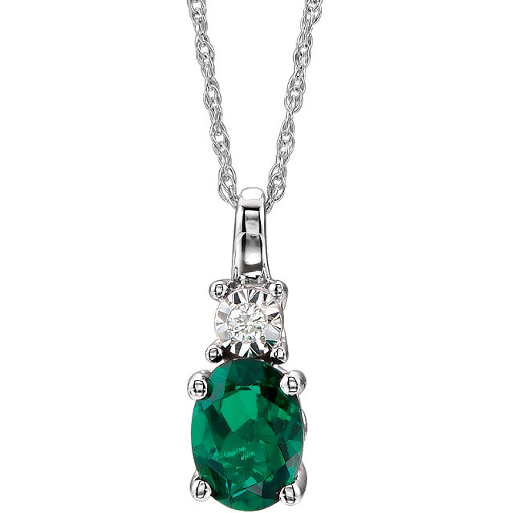 Exquisite 14Kt white gold pendant captures the beauty of a genuine 7x5mm oval Created Emerald accented by white shimmering diamonds hanging from an 18" inch necklace.Total weight of the diamonds is 0.02 total carat weight.
