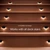 Close-up view of wooden deck stairs featuring small recessed lights along each step. The lights emit a soft white glow, highlighting the stair edges in a dark setting. Text on the image reads "Compatible by Design" and "Works with all deck stairs," emphasizing versatility. The overall scene focuses on outdoor safety and stylish accent lighting.