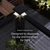 Close-up view of a contemporary deck railing illuminated at night. The scene shows a sleek post with integrated lights and horizontal cables overlooking a wooden deck and outdoor table. Lush plants and soft landscape lighting create a stylish outdoor living atmosphere. Text on the image reads "Outdoor Living After Dark" and "Designed to disappear by day and transform by night."
