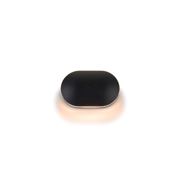 A small black oval object is centered against a clean white background. The item has smooth rounded edges and a matte surface. A soft warm glow surrounds its base, creating a subtle reflection and halo effect. The overall composition is minimal and modern, emphasizing shape and light.