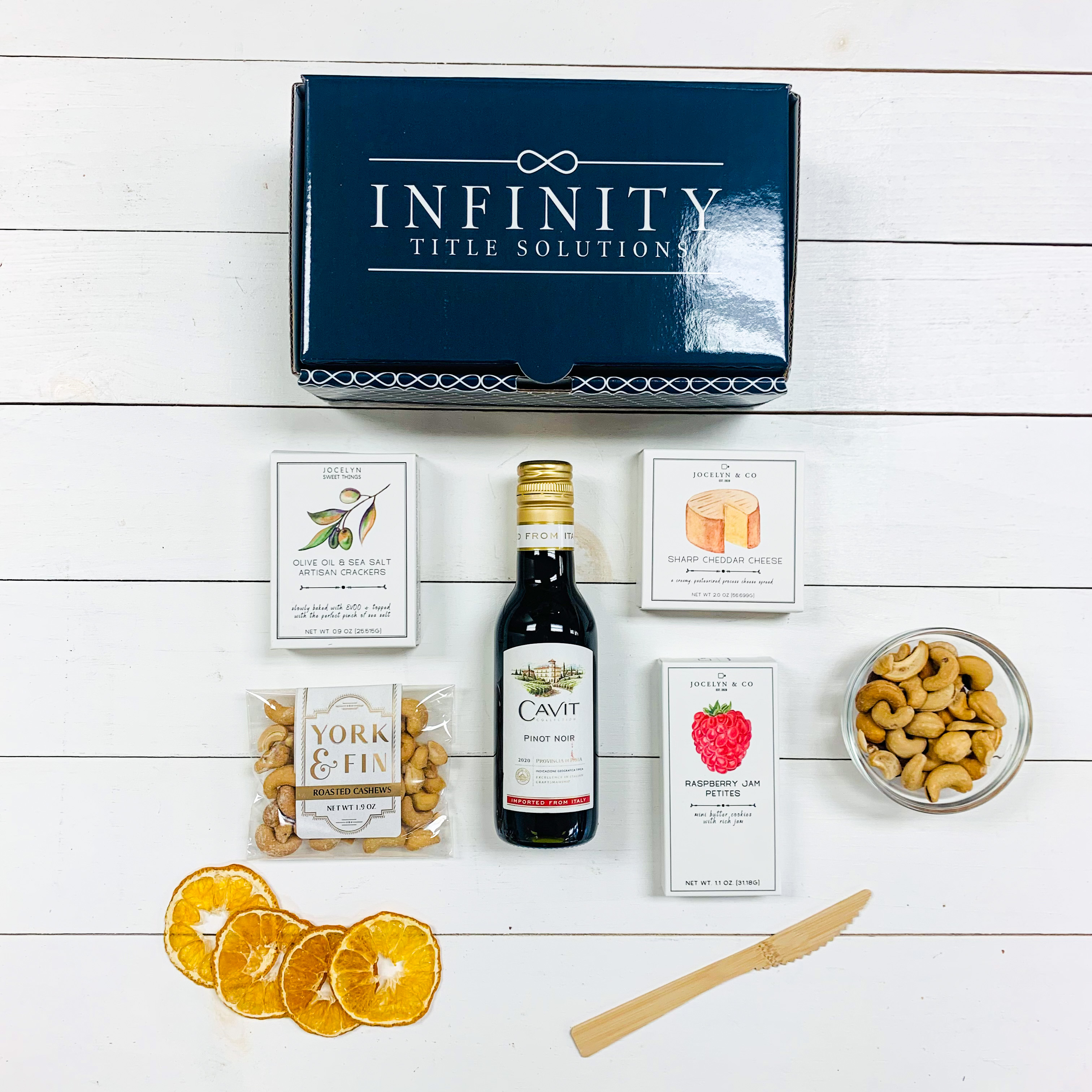 A navy rectangle box with the logo "Infinity Title Solutions" on it with 5 charcuterie items placed below