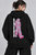 Female model wearing a black, regular-fit pullover hoodie with a kangaroo pocket. The chest features a graphic with the letters "KNSL" in a grey-to-hot-pink gradient inside a white rectangular border.