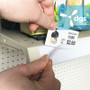 Self-Adhesive Shelf Info Data Strip Tag Holder, Clear with Black Back 1-1/4H x 48W shown on a gondola shelf edge at a retail store with a person inserting a price tag in it