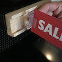 Person installing a sale sign into a wooden shelf molding price tag holder on a gondola shelf at a retail store