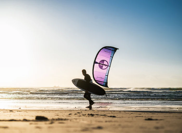Kitesurfer carrying a board and kite on the beach