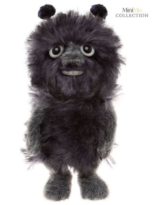 A dark grey fluffy monster-like teddy bear stands upright against a white background, featuring large round eyes, a slight smile, small round ears, and stubby feet.