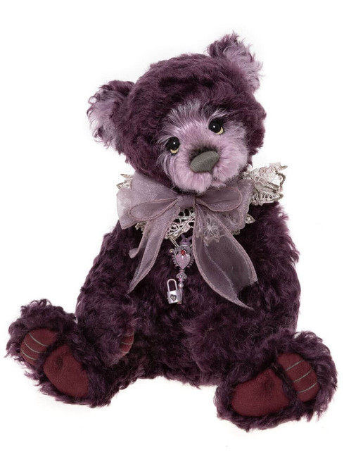 A deep purple/plum Charlie Bear sits upright, adorned with a grey organza bow, lace collar, and a silver heart-and-padlock charm pendant. Paws feature dark burgundy suede pads.
