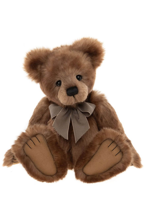 A brown plush teddy bear sits upright against a white background, wearing a small houndstooth bow tie, with large flat feet extended forward.
