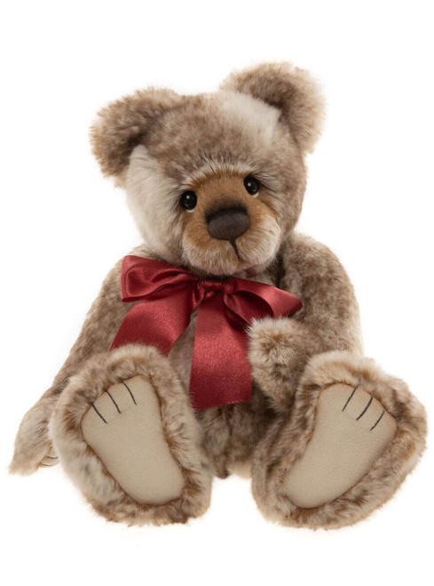 A plush Charlie Bear teddy sits upright, featuring mottled beige-brown fur, oversized paws facing forward, dark eyes, and a shiny red satin bow tied at its neck.