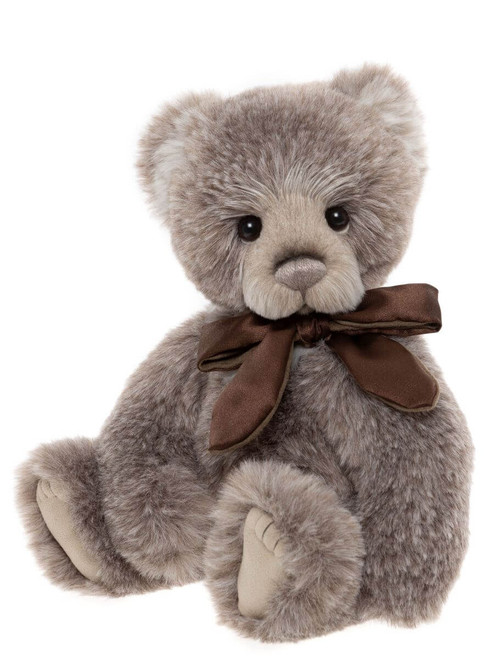 A grey-brown plush teddy bear sits upright against a white background, wearing a dark brown satin ribbon bow tied around its neck.