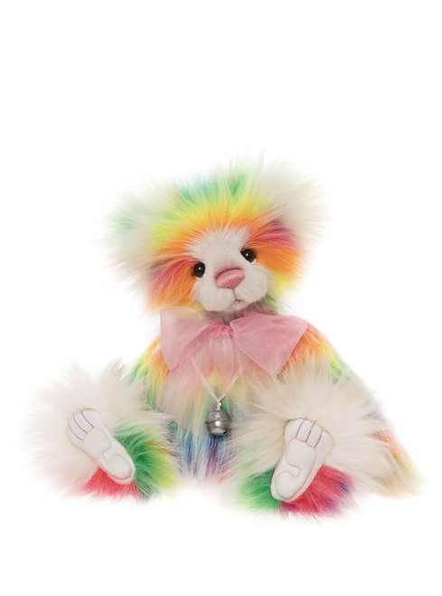 A rainbow tie-dye patterned Charlie Bear teddy sits upright, featuring multicoloured fur in pink, yellow, green, orange, and blue, with a pink bow and small silver bell around its neck.