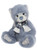A blue-grey plush teddy bear sits upright, wearing a blue plaid bow-tied scarf with white fringed ends, featuring a light blue nose and embroidered paw pads.