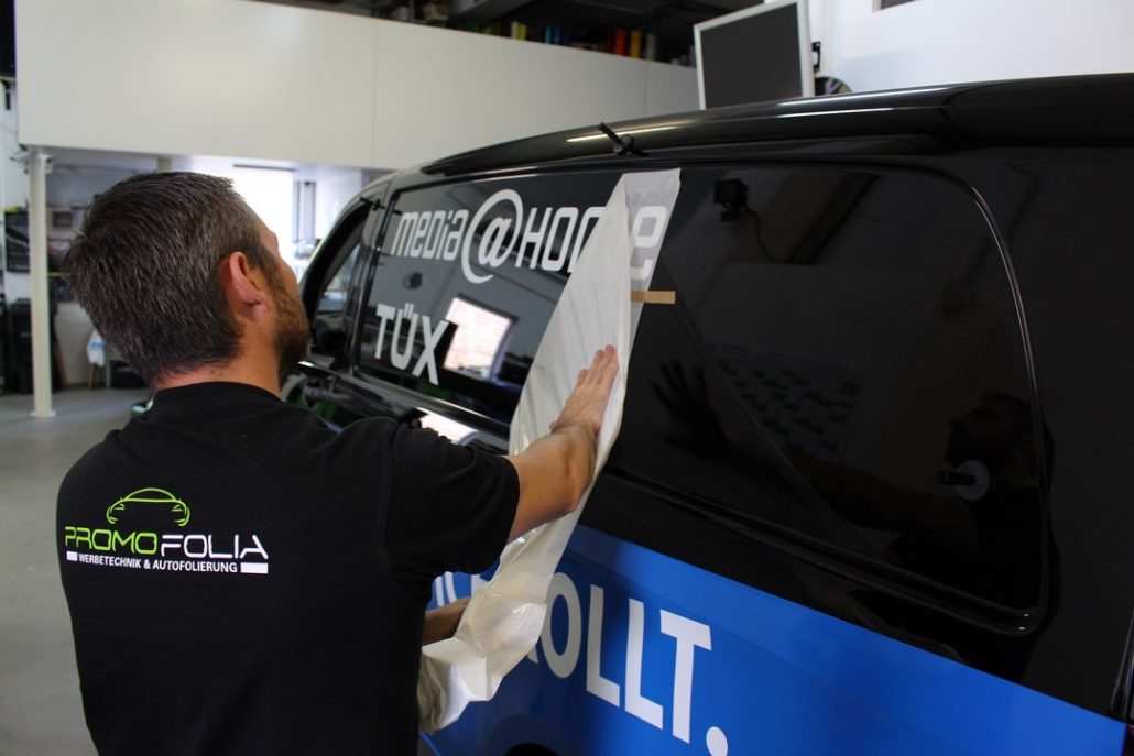 Promofolia installer applying vehicle lettering and graphics to a van